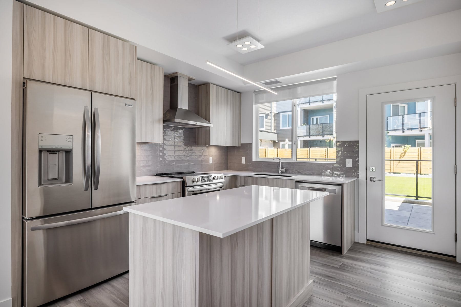 Kitchen in unit 103 at Green Square, Kelowna, with a quartz island, stainless appliances and the door to the patio