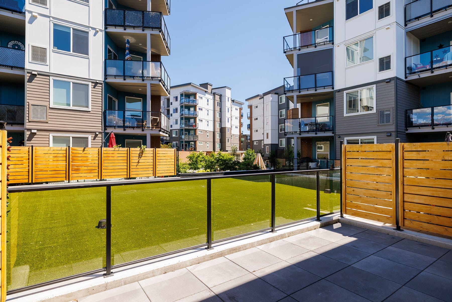 Fenced turf patio with a glass rail and cedar fence at unit 103, Green Square in Lower Mission, Kelowna