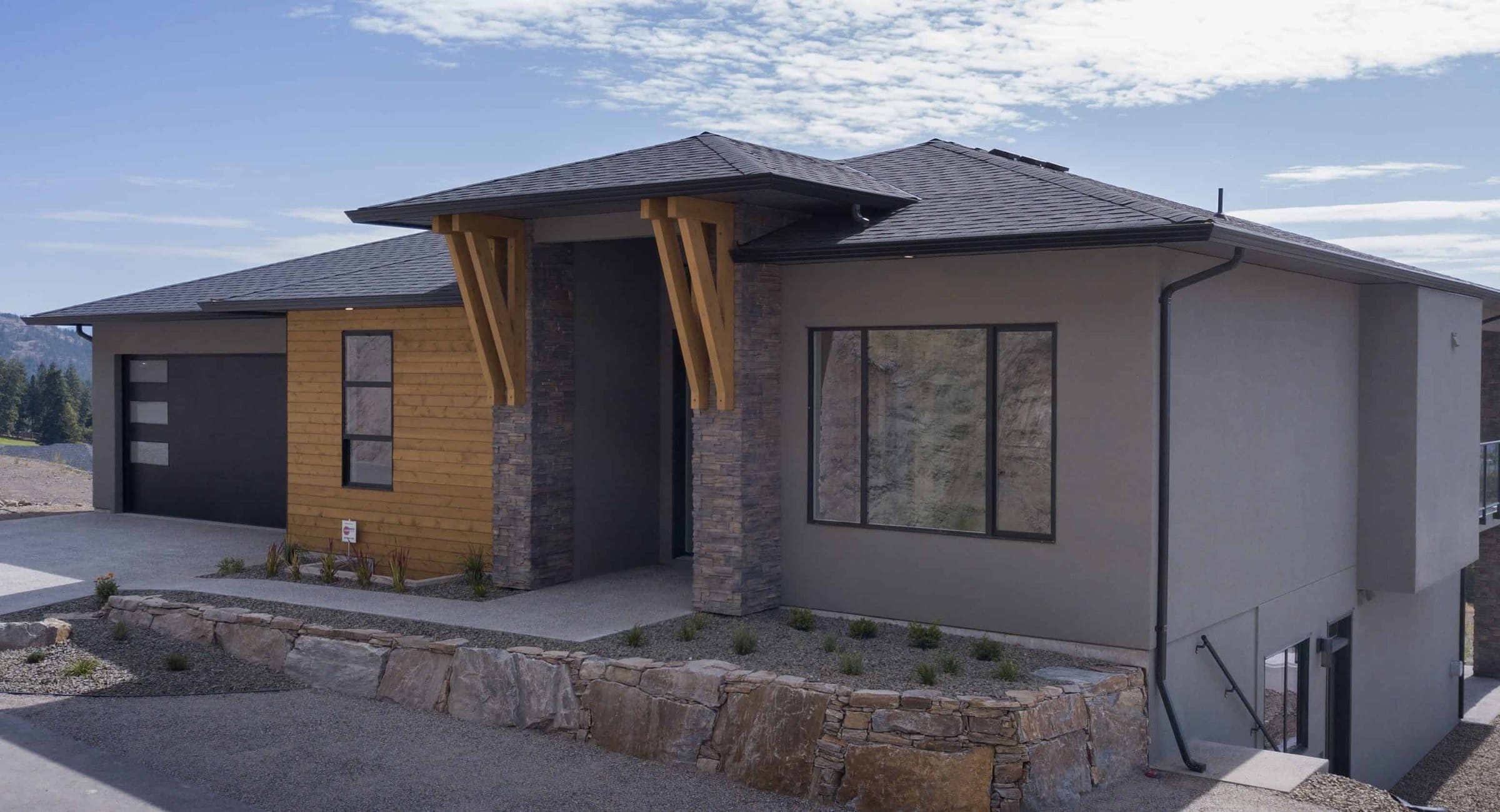 A finished Tallus Ridge home in West Kelowna with timber brackets over the stone entry and a double garage